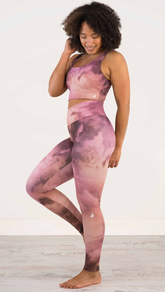 Full body side view of model wearing WERKSHOP Rose Quartz Athleisure Leggings. The leggings are printed with a warm rose/mauve and peachy watercolor effect with our eagle logo printed on the wearers outside left calf.
