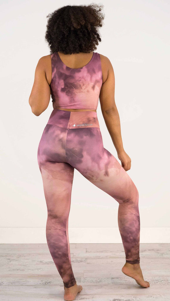 Full body back view of model wearing WERKSHOP Rose Quartz Athleisure Leggings. The leggings are printed with a warm rose/mauve and peachy watercolor effect with our eagle logo printed on the wearers outside left calf.
