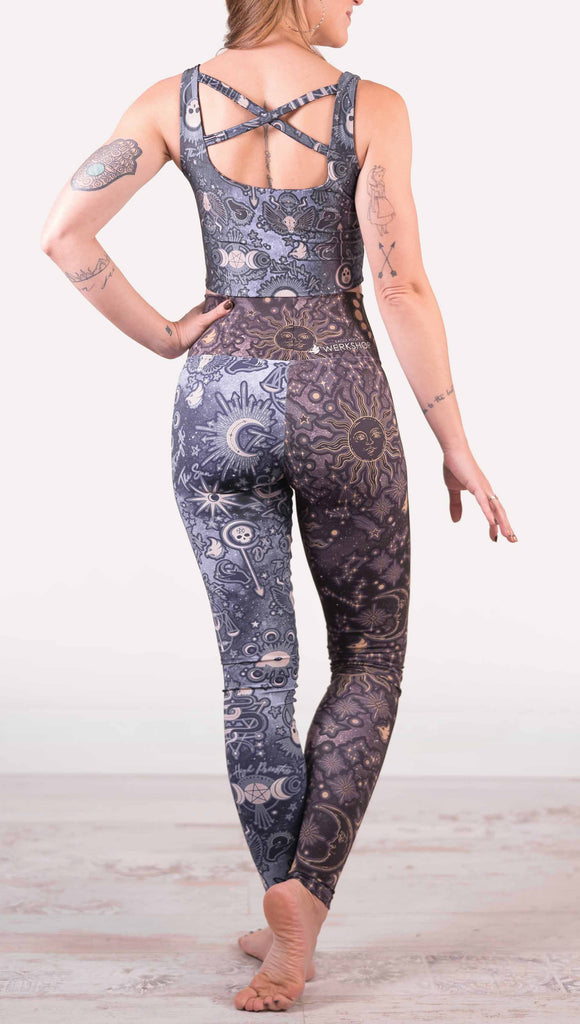 Model wearing WERKSHOP Zodiac and Tarot Mashed up Athleisure Leggings. The wearer’s right leg features zodiac themed artwork with the sun and moon with the moon phases, shooting stars and all 12 zodiac constellations in gold over a dark purple background. The left leg blue/tarot artwork has skulls, snakes, moons and the names of popular cards in the deck.