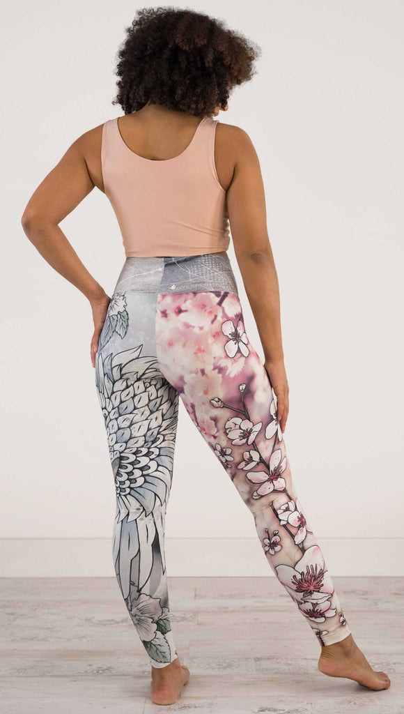 Full body back view of model wearing WERKSHOP Zen Mashup Athleisure Leggings. The leggigns are printed with pink cherry blossoms on the wearer's left leg and a graceful swooping crane on the opposite leg. There is also an abstract outline drawing of a koi fish on the waistband.