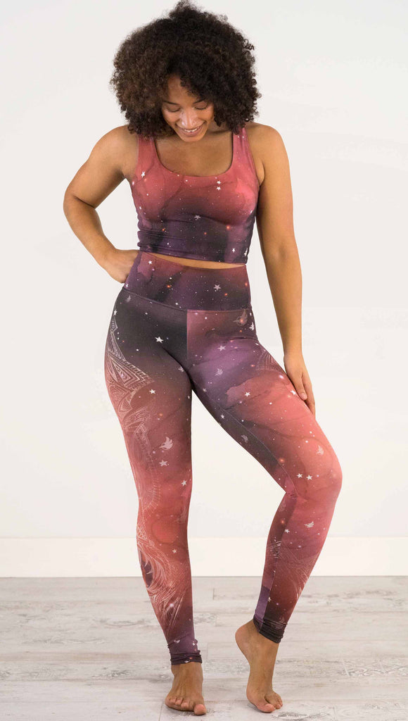 Full body front view of model wearing a red, orange and purple galaxy themed athleisure leggings with white henna inspired art running along the right side of the leg