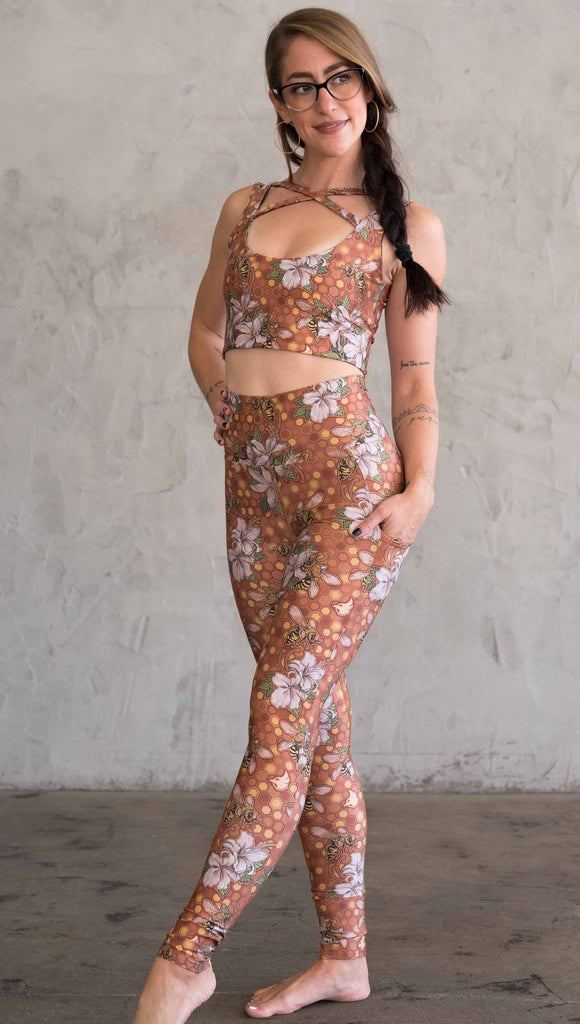 Full body view of model wearing ultra lightweight "featherlight" leggings with clusters of honeybees and flowers. Her hand is in the side pocket that is big enough to hold a phone. 