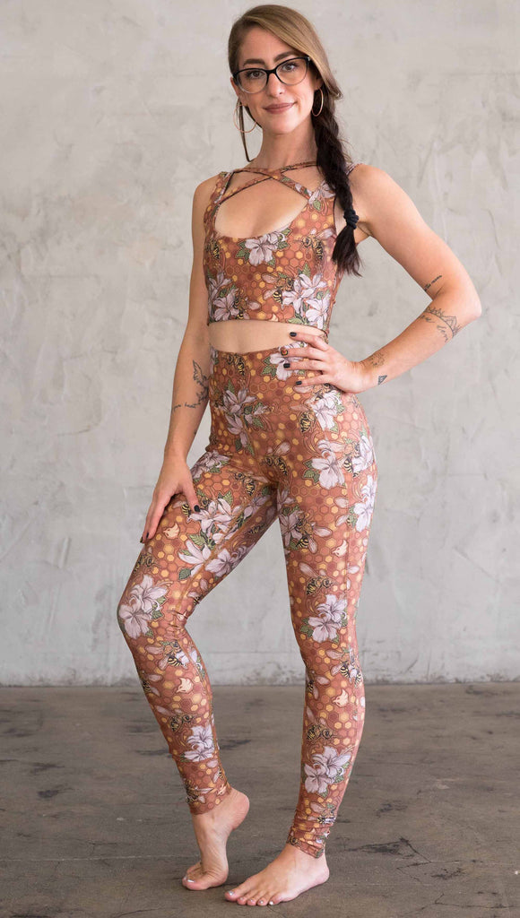Full body view of model wearing ultra lightweight "featherlight" leggings with clusters of honeybees and flowers. Her hand is in the side pocket that is big enough to hold a phone. 