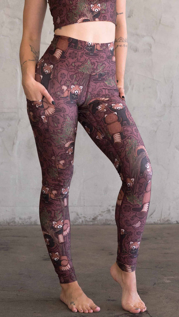 Front view of model wearing WERKSHOP Red Panda Leggings. The artwork is dark red with clusters of cute red pandas playing on trees. The leggings have phone pockets on both legs.