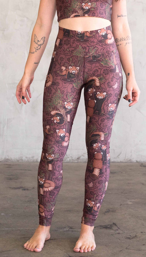 Front view of model wearing WERKSHOP Red Panda Leggings. The artwork is dark red with clusters of cute red pandas playing on trees. The leggings have phone pockets on both legs.
