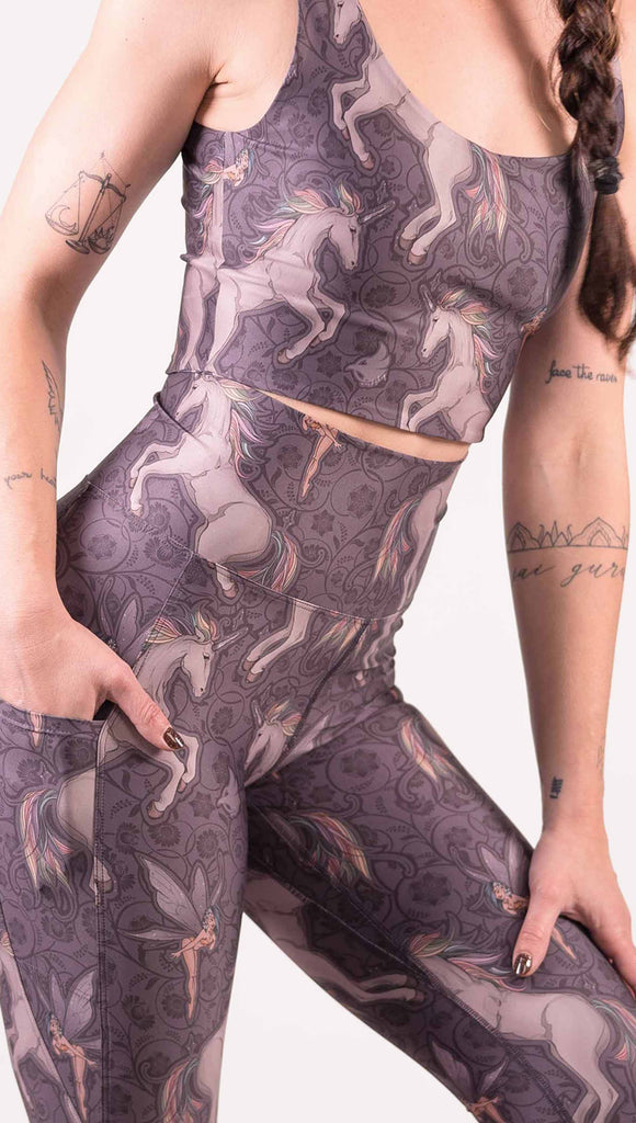 Zoomed in front view of model wearing WERKSHOP featherlight featherlight leggings with Original Unicorn artwork. The unicorns have soft rainbow colored hair and a small pixie friend over a purple background. The leggings have large pockets on each hip large enough to hold a phone.