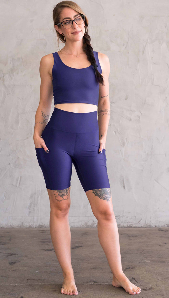 Model wearing WERKSHOP bicycle length shorts in featherlight fabric. Navy color with side cell phone pockets and a small eagle logo on the wearers left side
