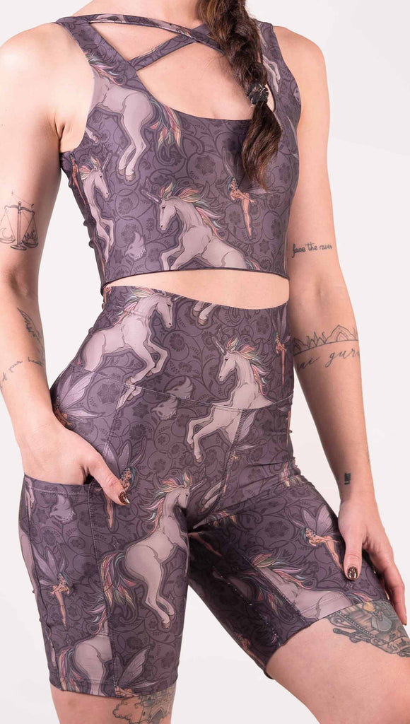 Zoomed in view of model wearing WERKSHOP featherlight bicycle length shorts with Original Unicorn artwork. The unicorns have soft rainbow colored hair and a small pixie friend over a purple background. The shorts have large pockets on each hip large enough to hold a phone.