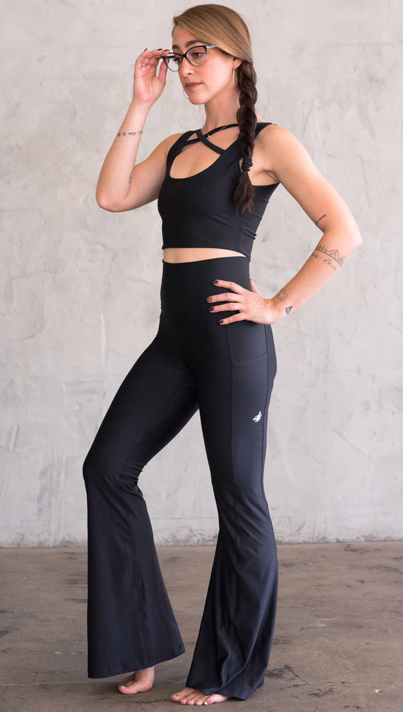 Full Body side view of model wearing WERKSHOP Featherlight Bell Bottoms in solid black. The bells have a small reflective eagle logo on the wearer's left side pocket.