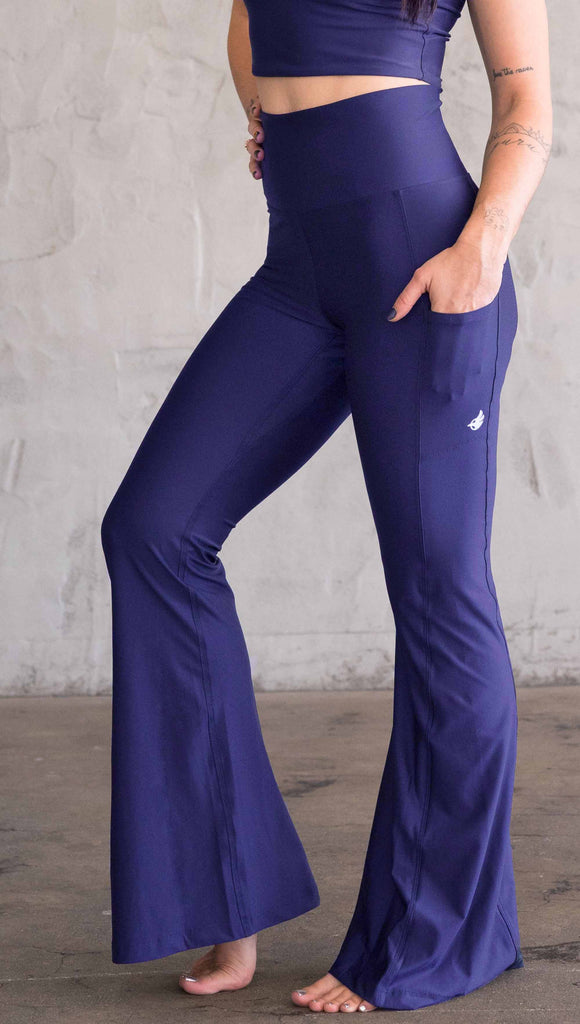 Model wearing WERKSHOP Royal Blue Featherlight Bells. They are a bright blue color with a flared leg opening, pockets on the hip, have a high waistband and a flattering long panel gusset.