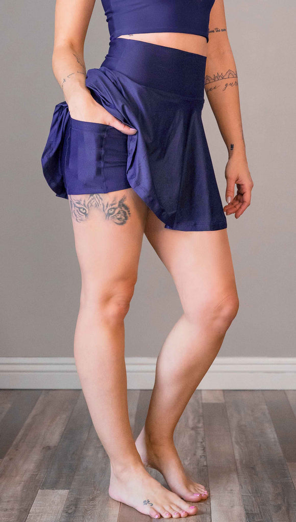 model wearing WERKSHOP Tennis Skirt, with the skirt lifted up to show the shorts and pockets underneath. In solid royal blue color