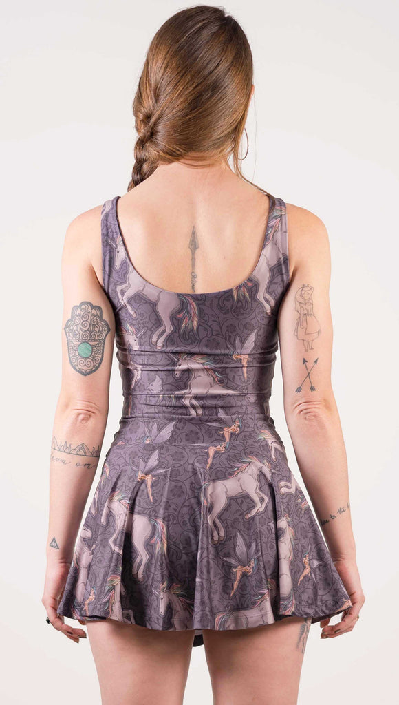 Back view of model wearing WERKSHOP Four-Way Reversible Top with Original Mermaids artwork on one side and Unicorn artwork on the opposite side. She is shown wearing the unicorns on the outside with the “X” strap detail in the front. The unicorns have soft rainbow-colored hair with a pixie friend over a purple background.