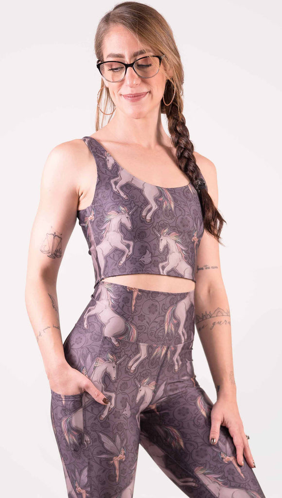 Front view of model wearing WERKSHOP Four-Way Reversible Top with Original Mermaids artwork on one side and Unicorn artwork on the opposite side. She is shown wearing the unicorns on the outside with the “X” strap detail in the back. The unicorns have soft rainbow-colored hair with a pixie friend over a purple background.