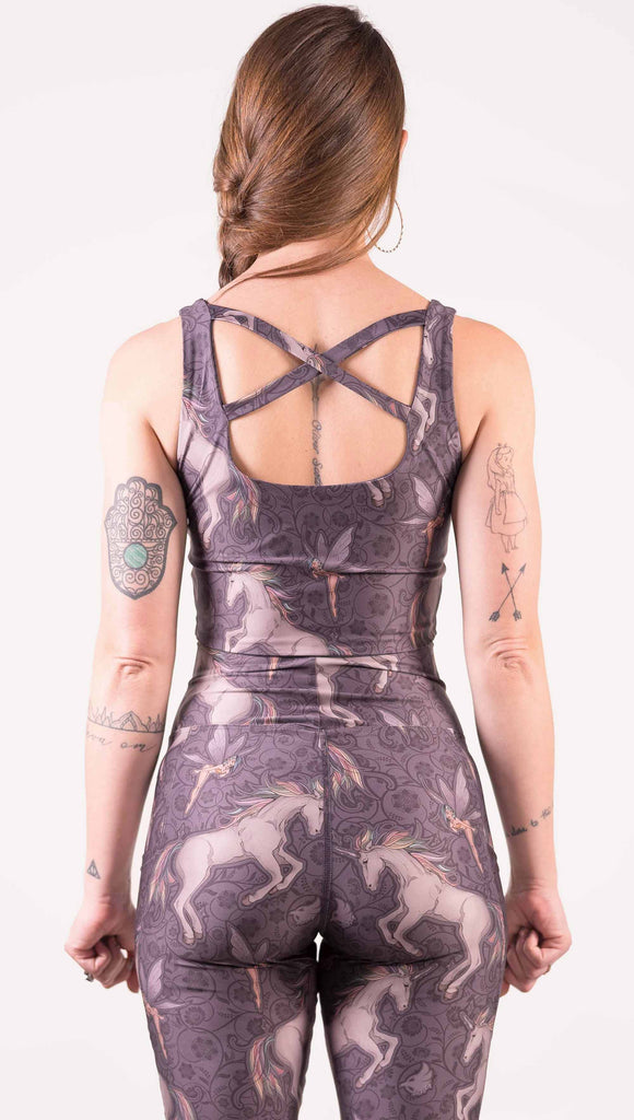 Back view of model wearing WERKSHOP Four-Way Reversible Top with Original Mermaids artwork on one side and Unicorn artwork on the opposite side. She is shown wearing the unicorns on the outside with the “X” strap detail in the back. The unicorns have soft rainbow-colored hair with a pixie friend over a purple background.