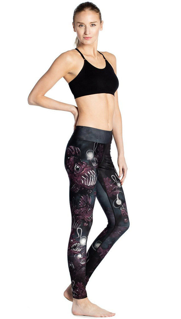 model standing slightly sideways wearing deep sea angler fish printed full length leggings and black sports top