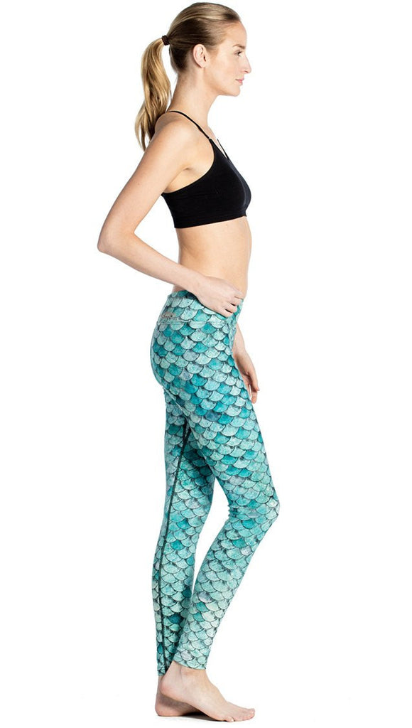 right side view of model wearing teal mermaid / fish scale printed full length leggings