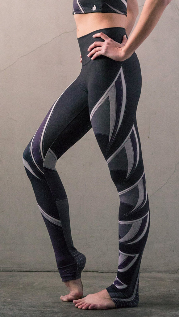 Left side view of model wearing black printed full-length leggings with purple and gray stripe design