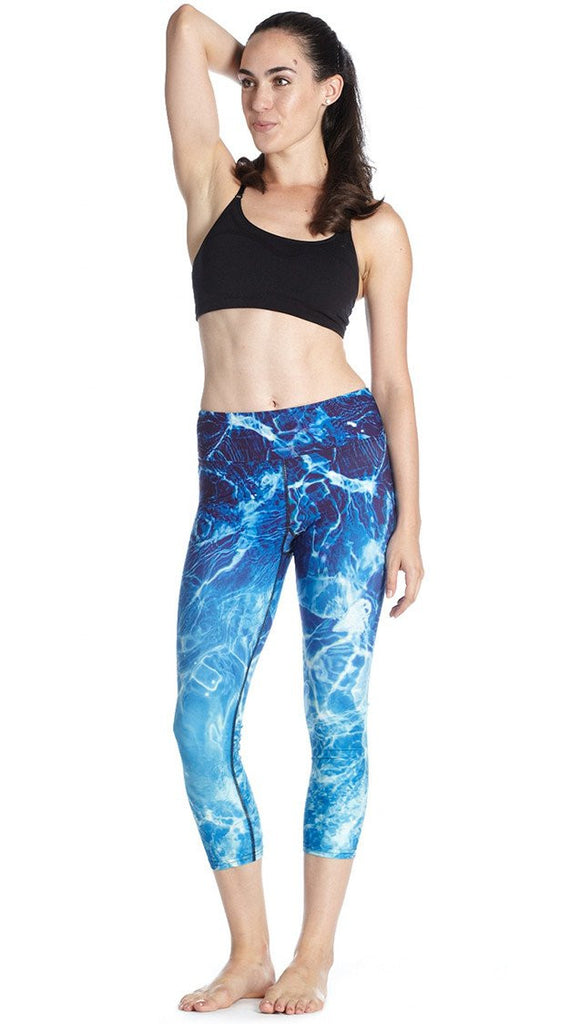 front view of model wearing water / ocean themed printed capri leggings and black sport top