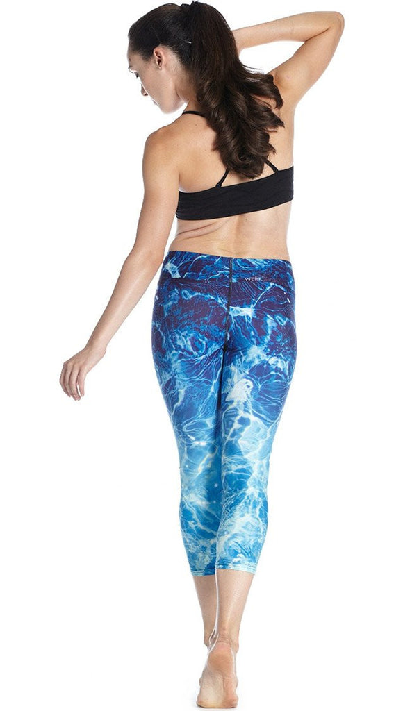 back view of model wearing water / ocean themed printed capri leggings and black sport top