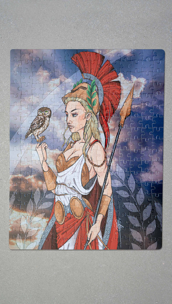 Full view of WERKSHOP Athena Puzzle. image of WERKSHOP Athena artwork printed on a 252 piece jigsaw puzzle. The artwork features Athena, the goddess of war standing on a cliff’s edge. She is holding a spear with one hand and her owl with the other. She is wearing a greek goddess dress/warrior hat with colors of cream, gold and red. Behind her is a beautiful cloudy sky with rays of light shining down onto her. The model is also wearing a matching top.