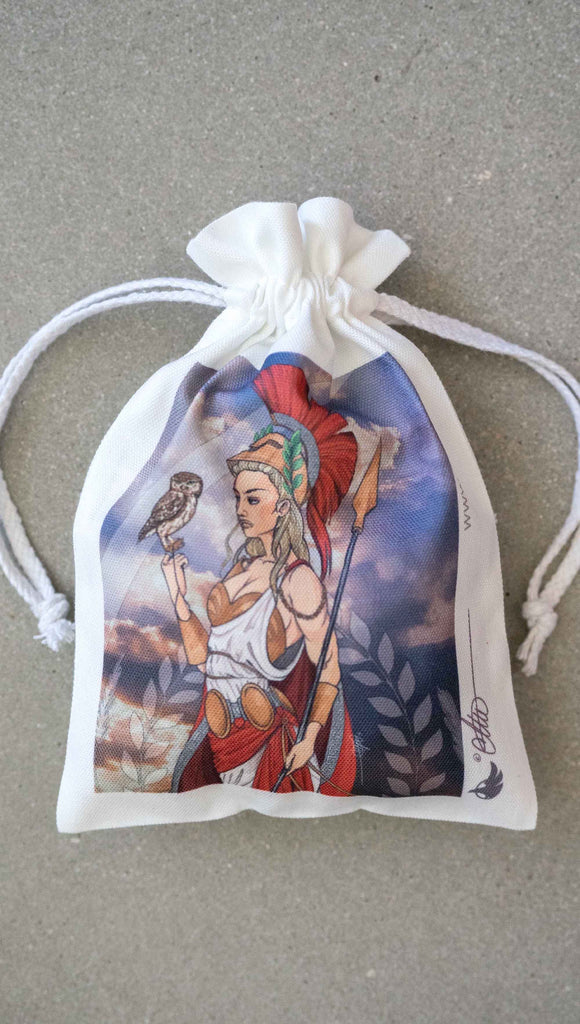 Canvas drawcord pouch (comes free with matching puzzle)! The artwork features Athena, the goddess of war standing on a cliff’s edge. She is holding a spear with one hand and her owl with the other. She is wearing a greek goddess dress/warrior hat with colors of cream, gold and red. Behind her is a beautiful cloudy sky with rays of light shining down onto her. The model is also wearing a matching top.