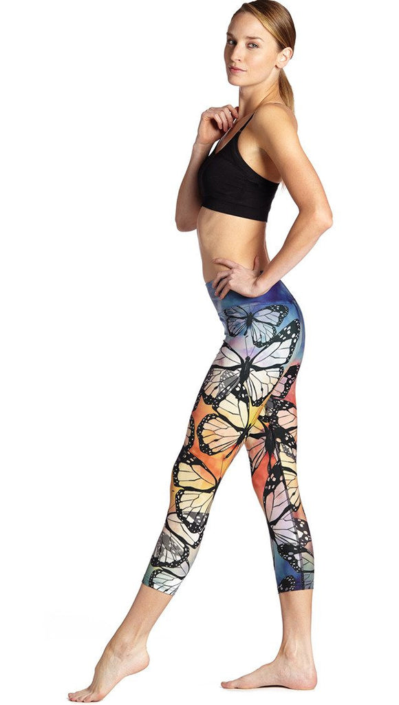 left side view of model wearing colorful butterfly themed printed capri triathlon leggings and sports top