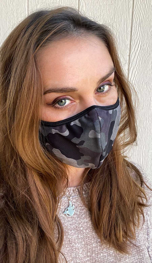Girl wearing WERKSHOP Camo Face Mask - classic green and brown colors with an orange logo and adjustable ear loops.
