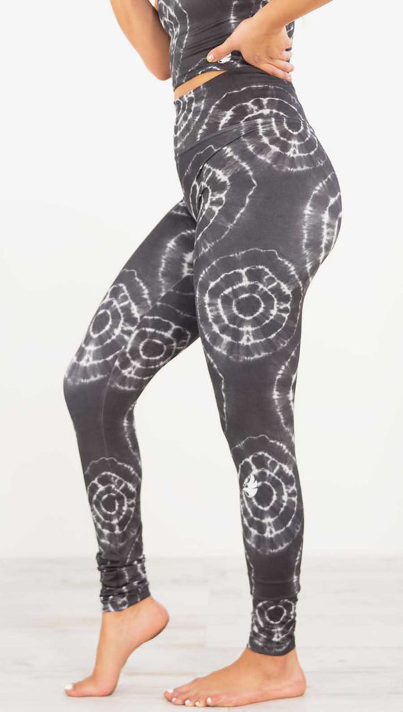 Left view of model wearing the charcoal athleisure leggings. It is in a charcoal color and has white tie dye circles throughout. Each circle has a smaller circle within each other