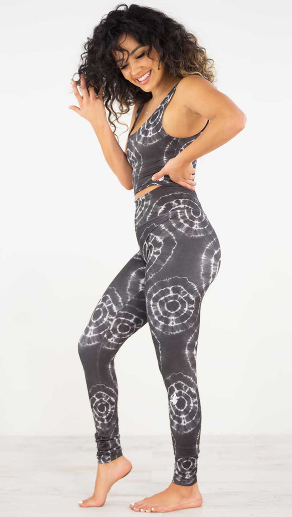 Left side view of model wearing the charcoal athleisure leggings. They are in a charcoal color and have white tie dye circles throughout. Each circle has a smaller circle within each other.