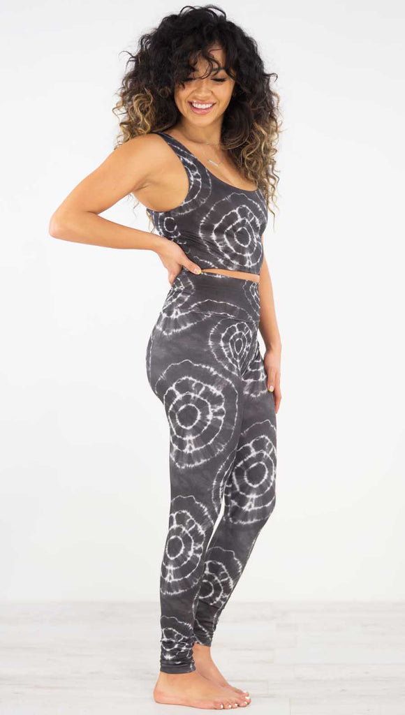 Right side view of model wearing the charcoal athleisure leggings. They are in a charcoal color and have white tie dye circles throughout. Each circle has a smaller circle within each other.