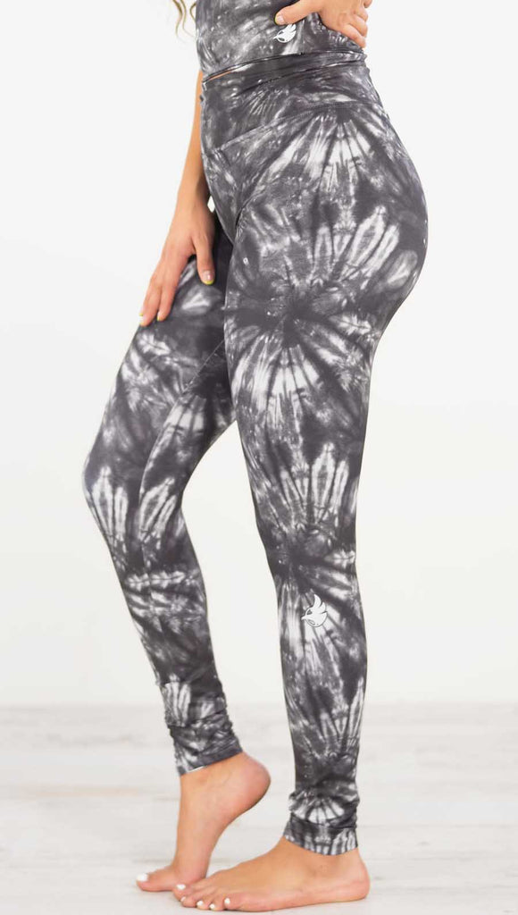 Left side view of model wearing the charcoal spiral athleisure leggings. They are in a charcoal color and have white tie dye spirals throughout the leggings.