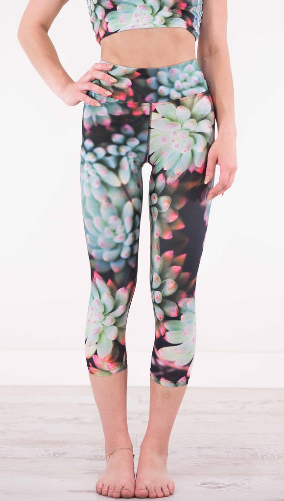 Front view of model wearing black capri leggings with green succulent plants with pink tips throughout