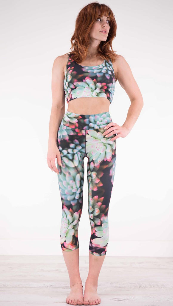 Front view of model wearing black capri leggings with green succulent plants with pink tips throughout and the matching top