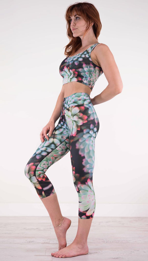 Left view of model wearing black capri leggings with green succulent plants with pink tips throughout and the matching top