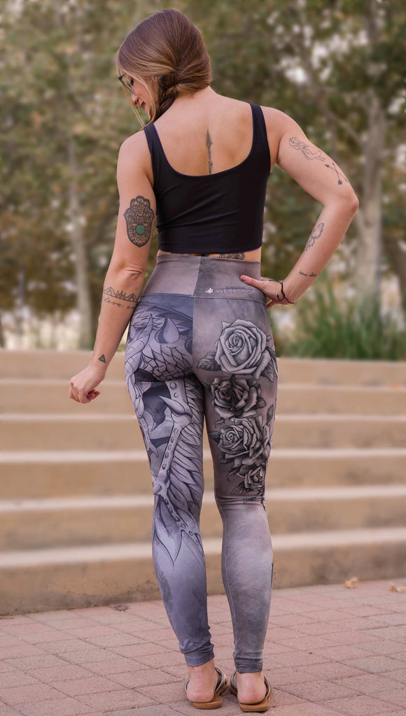 Model wearing WERKSHOP Dagger Mashup Leggings. One leg has a dagger with a wreath of roses. The other leg has an abstract gargoyle-esc dragon. Both legs are neutral in color tone with the right leg being a bit taupe and the left leg being a cool gray.