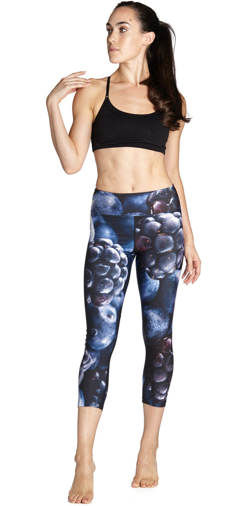 Model wearing leggings printed with a macro image of bluberries and blackberries. The colors are rich deep blues and purples.