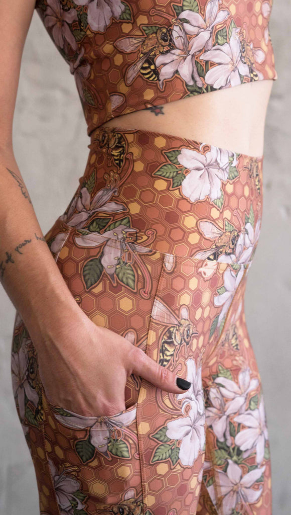 Zoomed in photo of model wearing ultra lightweight "featherlight" leggings with clusters of honeybees and flowers. Her hand is in the side pocket that is big enough to hold a phone. 