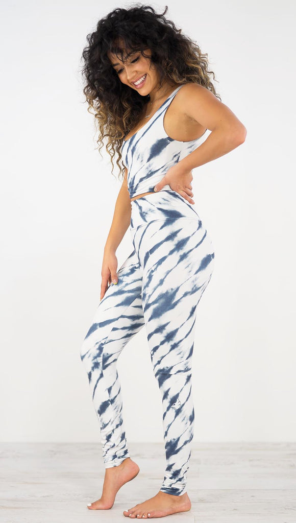 Left side view of model wearing the indigo stripes athleisure leggings. They are in a white color and have blue zebra-like stripes.