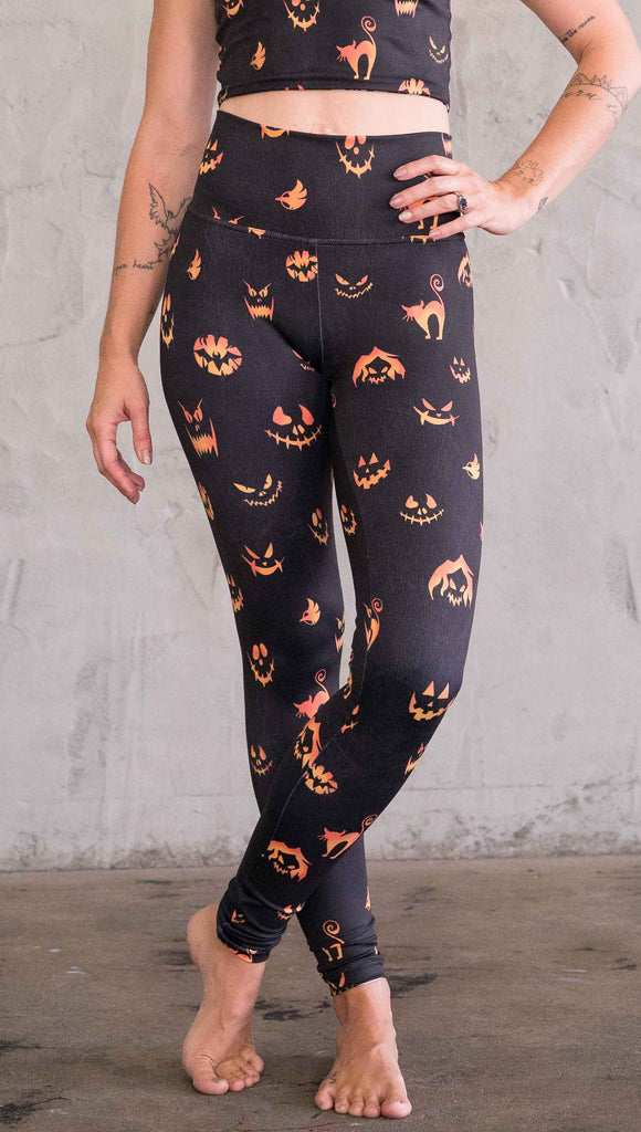 Front view of model wearing the black athleisure leggings with bright orange jack-o-lantern faces and cats throughout