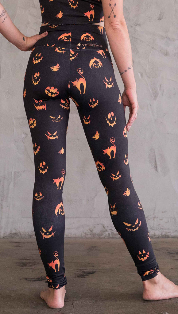 Back view of model wearing the black athleisure leggings with bright orange jack-o-lantern faces and cats throughout