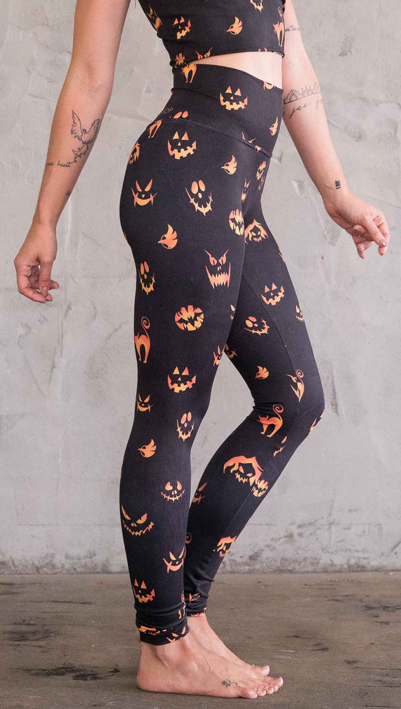 Right view of model wearing the black athleisure leggings with bright orange jack-o-lantern faces and cats throughout