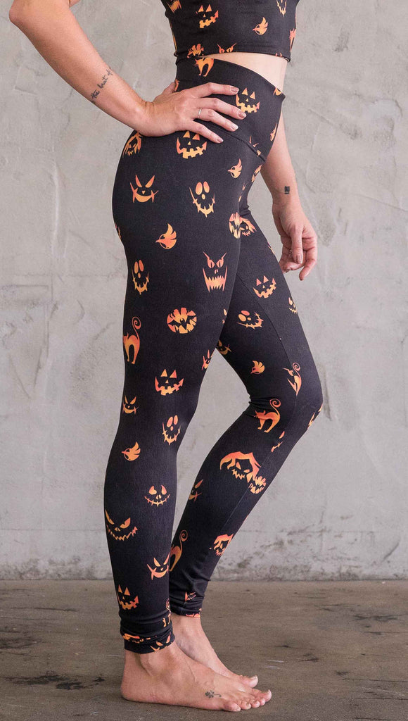 Right view of model wearing the black athleisure leggings with bright orange jack-o-lantern faces and cats throughout 
