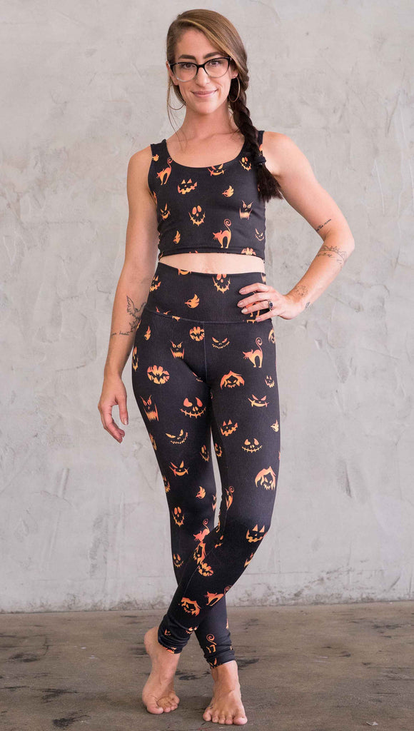 Front view of model wearing the black athleisure leggings with bright orange jack-o-lantern faces and cats throughout