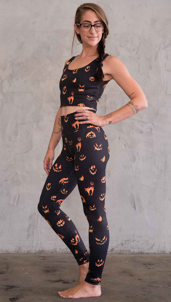Left view of model wearing the black athleisure leggings with bright orange jack-o-lantern faces and cats throughout