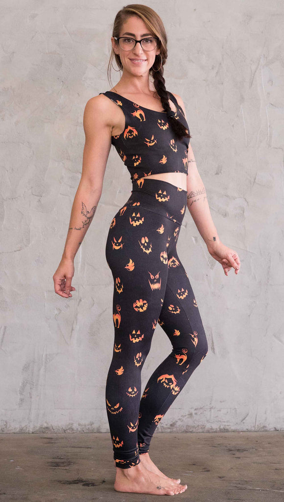 right view of model wearing the black athleisure leggings with bright orange jack-o-lantern faces and cats throughout