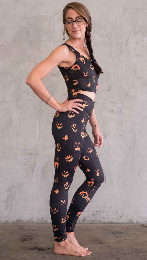 Right view of model wearing the black athleisure leggings with bright orange jack-o-lantern  faces and cats throughout