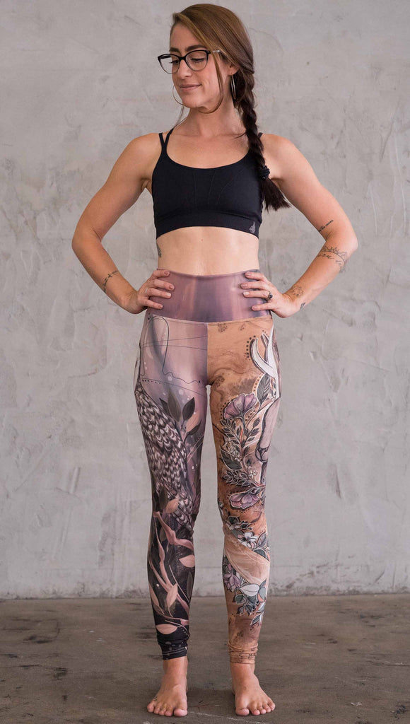 Zoomed out front view of model wearing the jackalope/ owl mashup leggings in a light mauve and brown color. One leg has an owl and the other leg has a jackalope