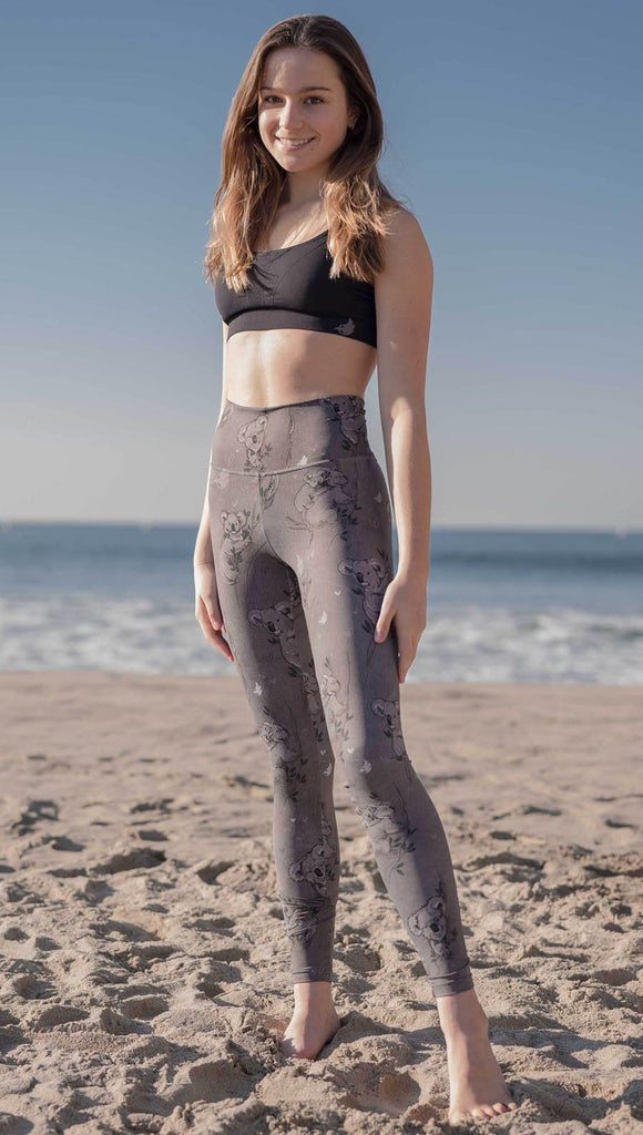 Front view of model wearing koala leggings with tree branches and leaves on the beach