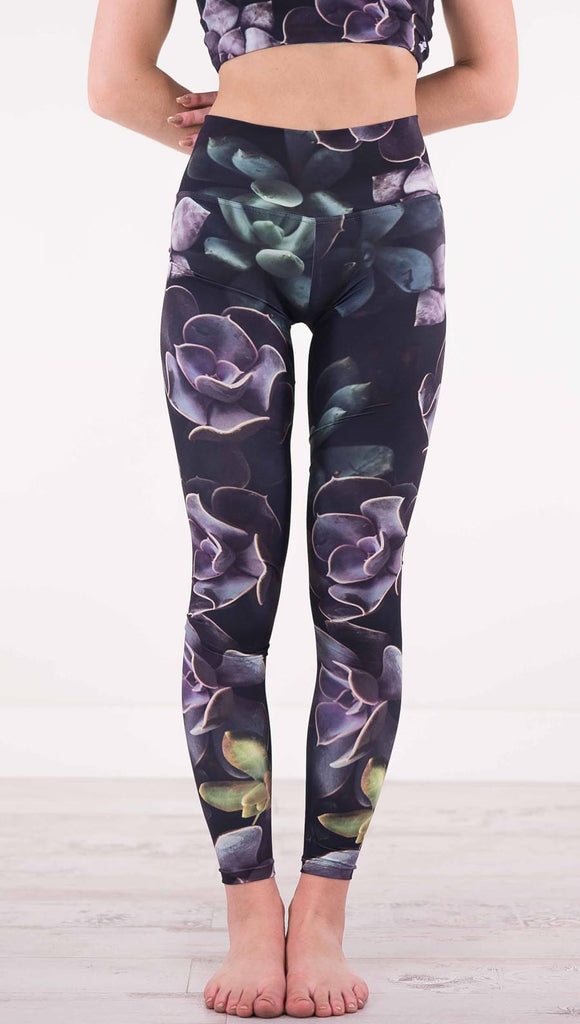 Front view of model wearing black athleisure leggings with green and purple succulent plants throughout