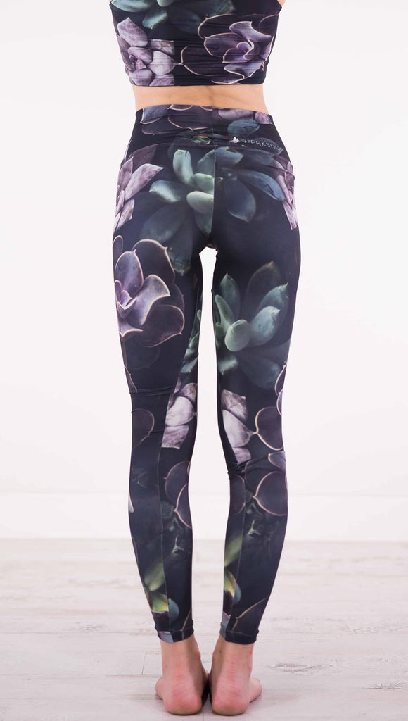 Enhanced back view of model wearing black athleisure leggings with green and purple succulent plants throughout